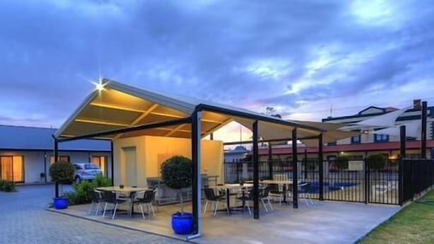 A modern building with a covered outdoor seating area, a parking lot, and a clear sky.