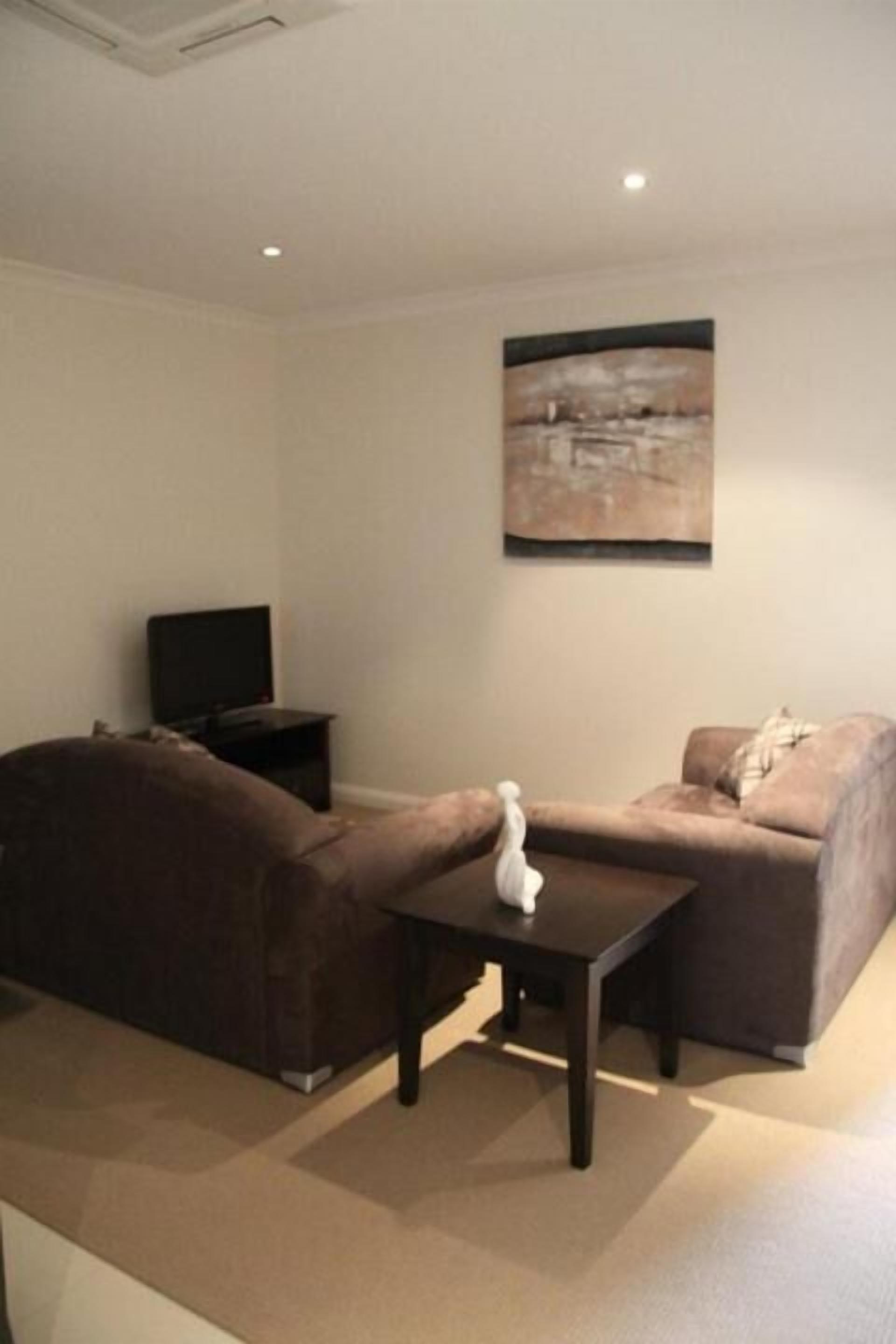 A living room with a brown sofa, a coffee table, and a television on a stand.
