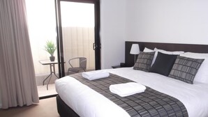 A hotel room with a large bed, a nightstand, a lamp, and a view of the outside balcony.