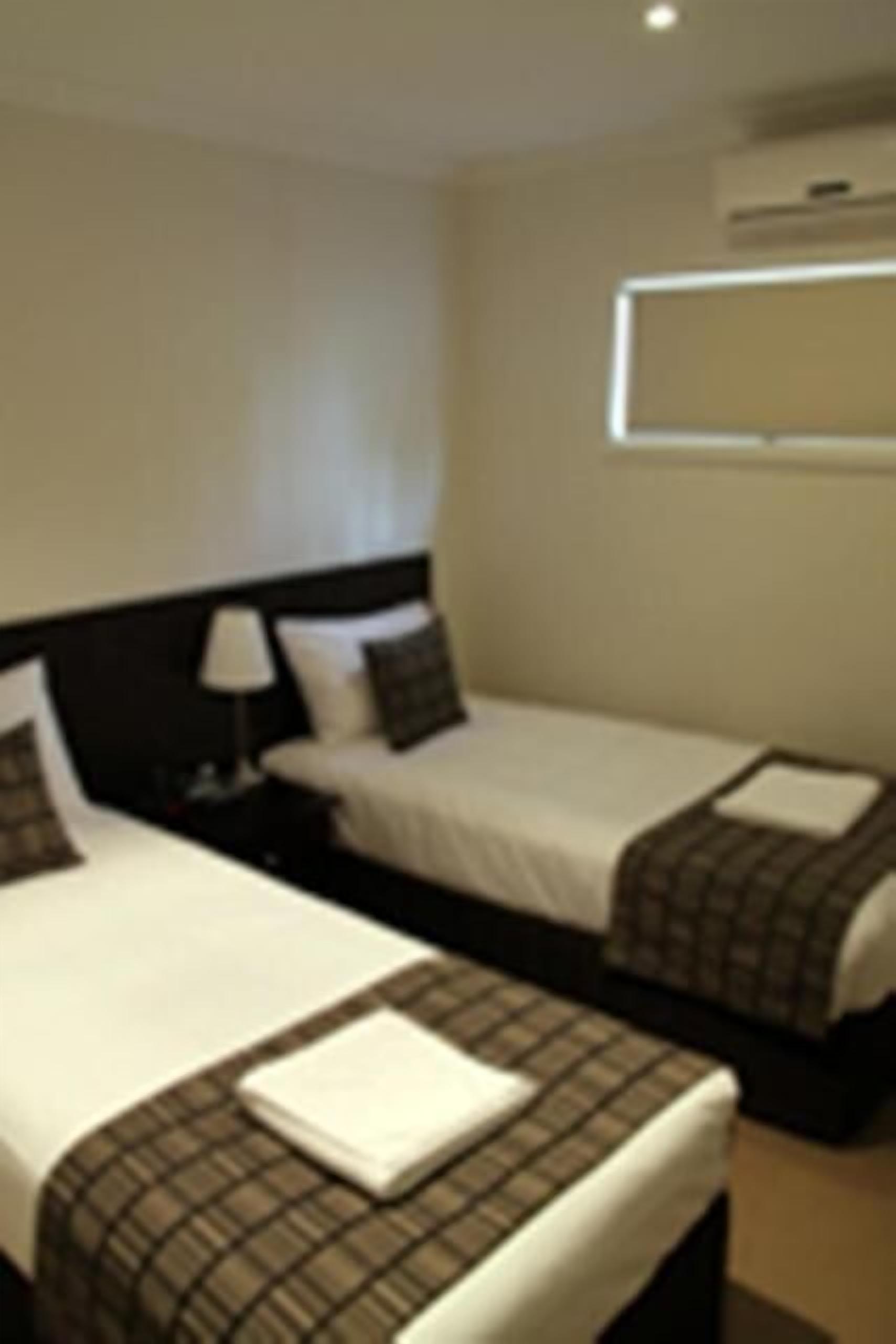 A hotel room with two beds, a nightstand, a lamp, and a window.