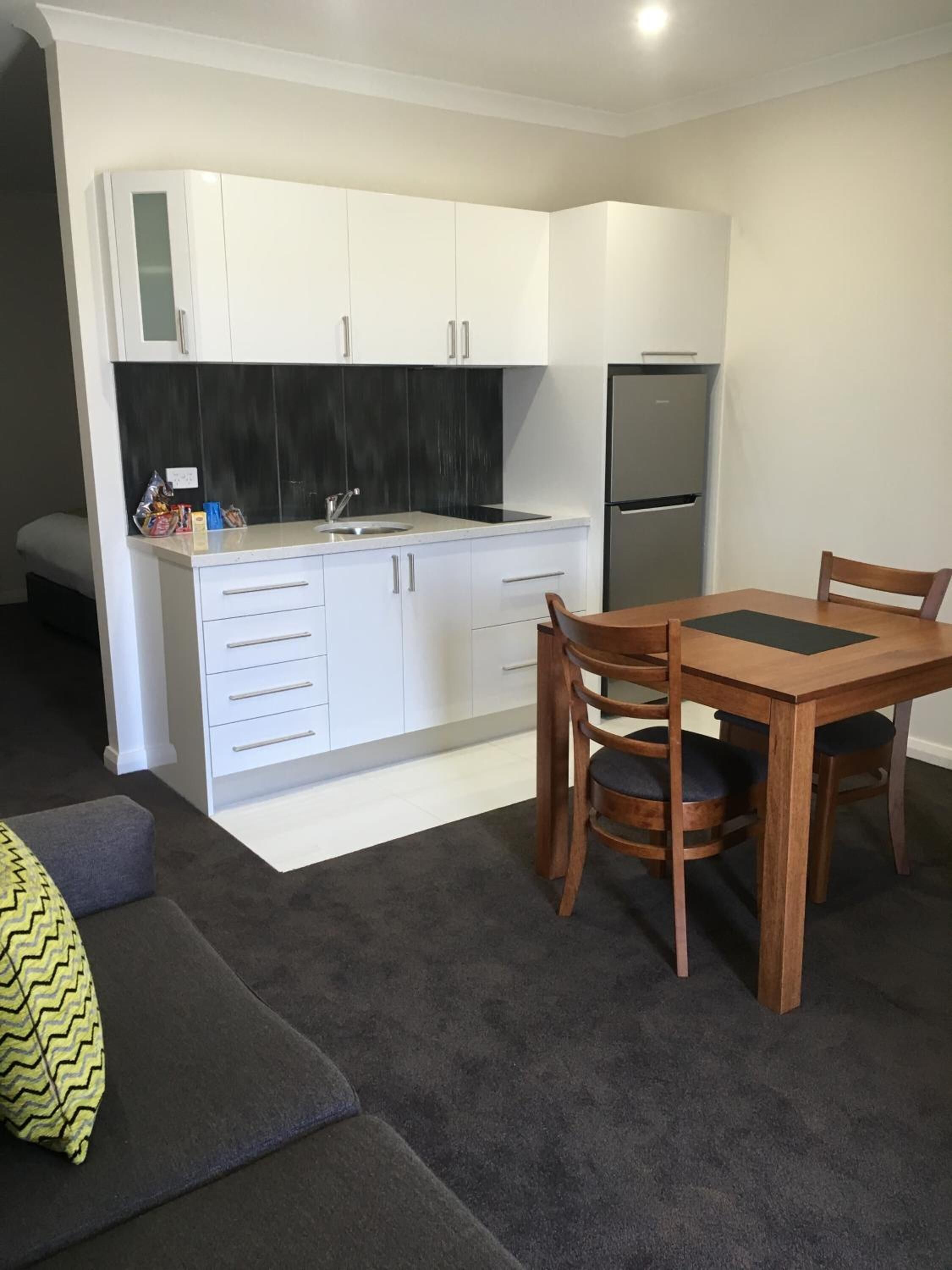 A compact kitchen with white cabinets, a black backsplash, and a stainless steel refrigerator.
