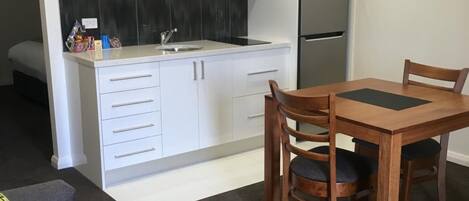 A compact kitchen with white cabinets, a black backsplash, and a stainless steel refrigerator.