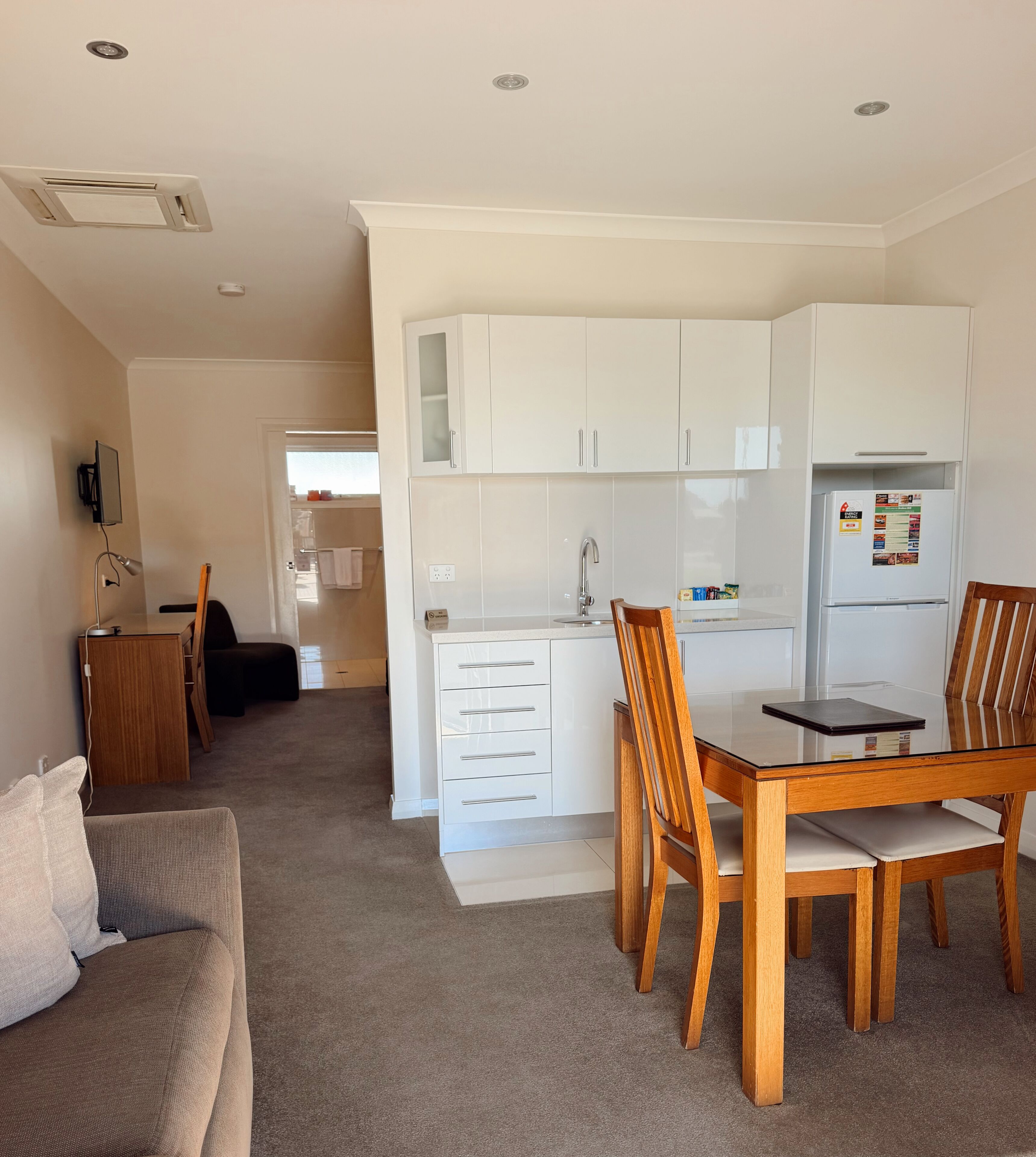 A compact kitchen with white cabinets, a dining table with chairs, a built-in oven, and a refrigerator.