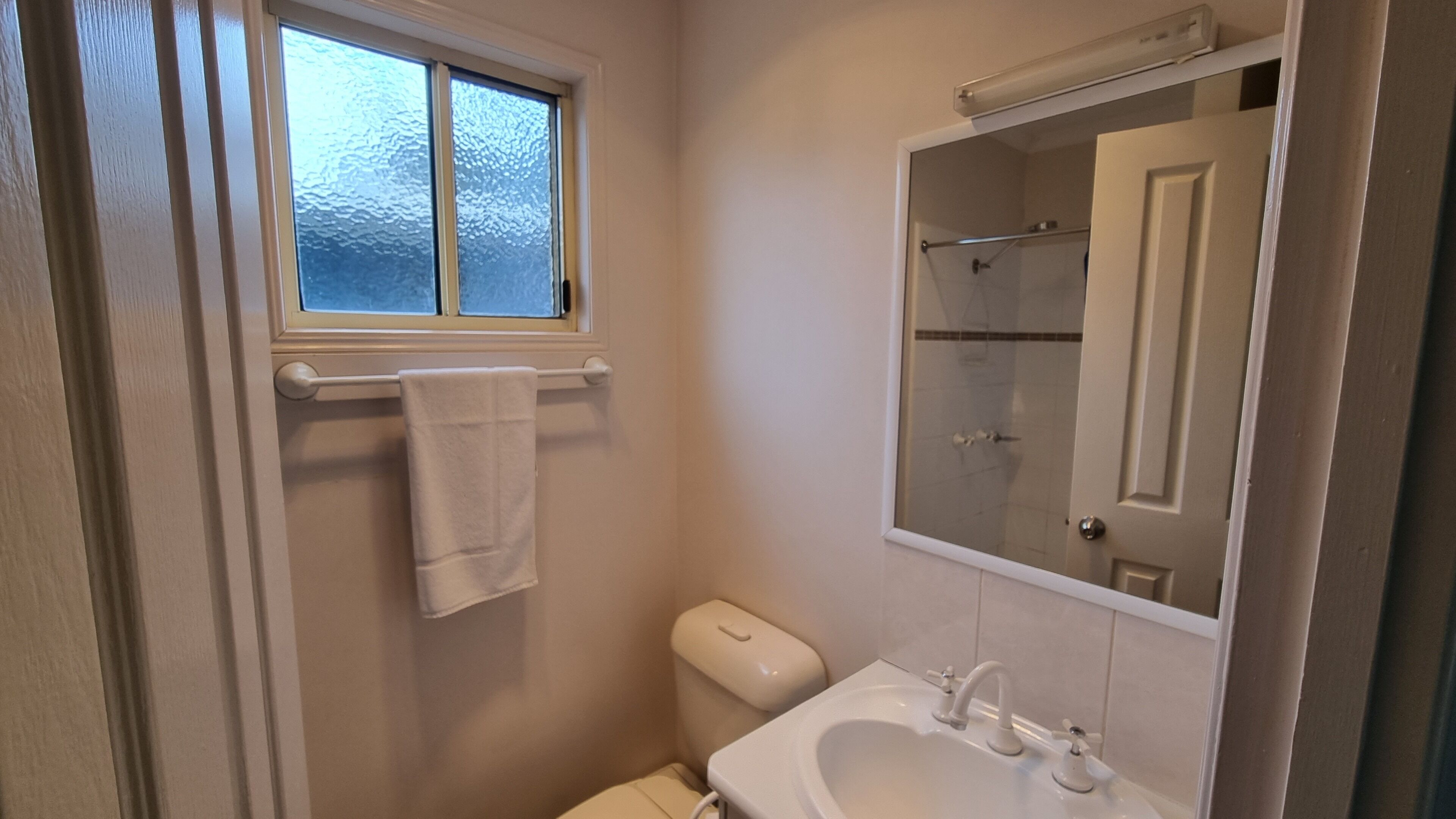 A small bathroom with a toilet, sink, and a window above the toilet.