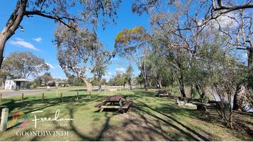 A park with picnic tables, a small building, and a fenced area.
