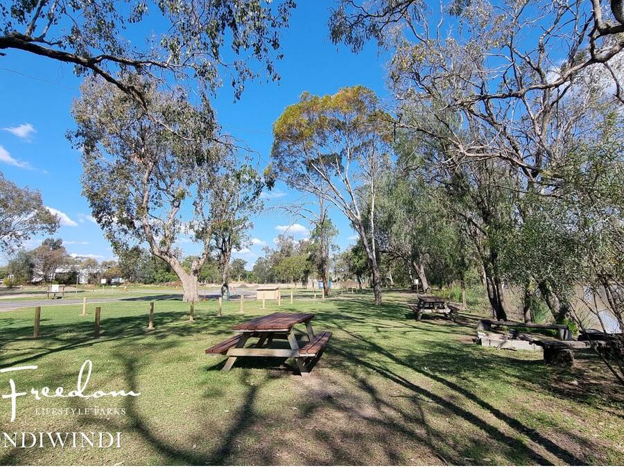 A park with picnic tables, a small building, and a fenced area.