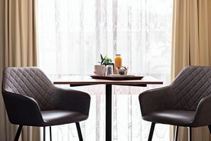 A dining area with two black chairs and a table set with a mug, a glass, a plate with food, a plant, and a bottle of juice.
