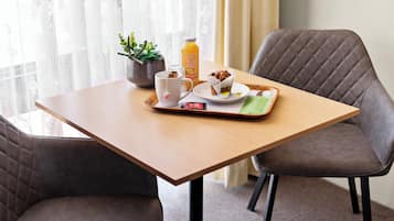 A neatly arranged breakfast tray on a wooden table with a cup, a bottle of juice, a plate with a pastry, and a small potted plant.