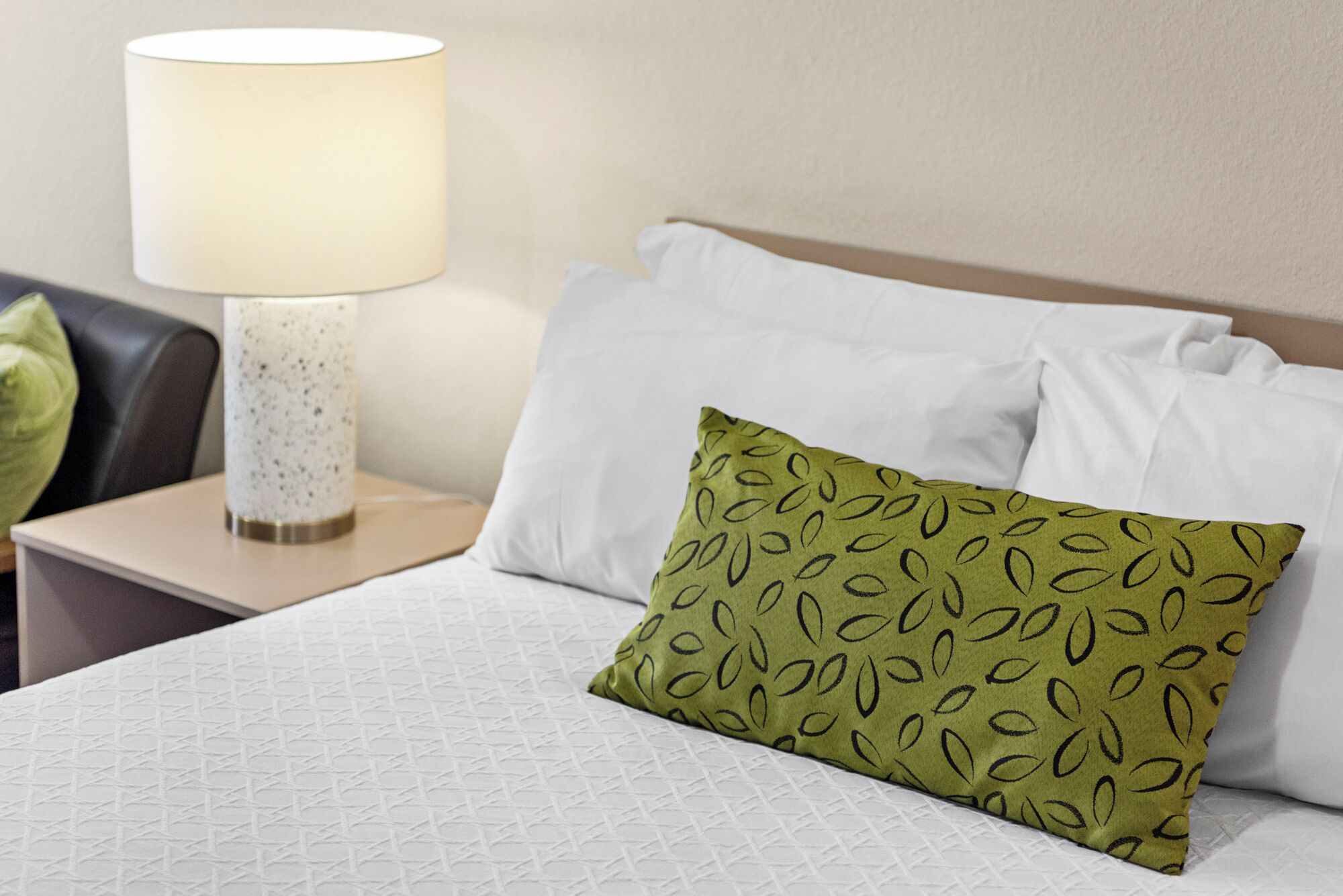 A neatly made bed with white linens and a green pillow with a leaf pattern.