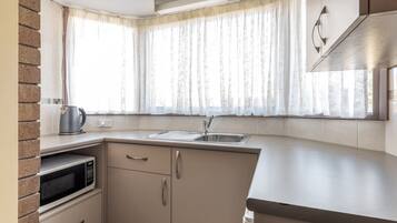 Cocina compacta con microondas, lavabo y ventana con cortinas translúcidas.