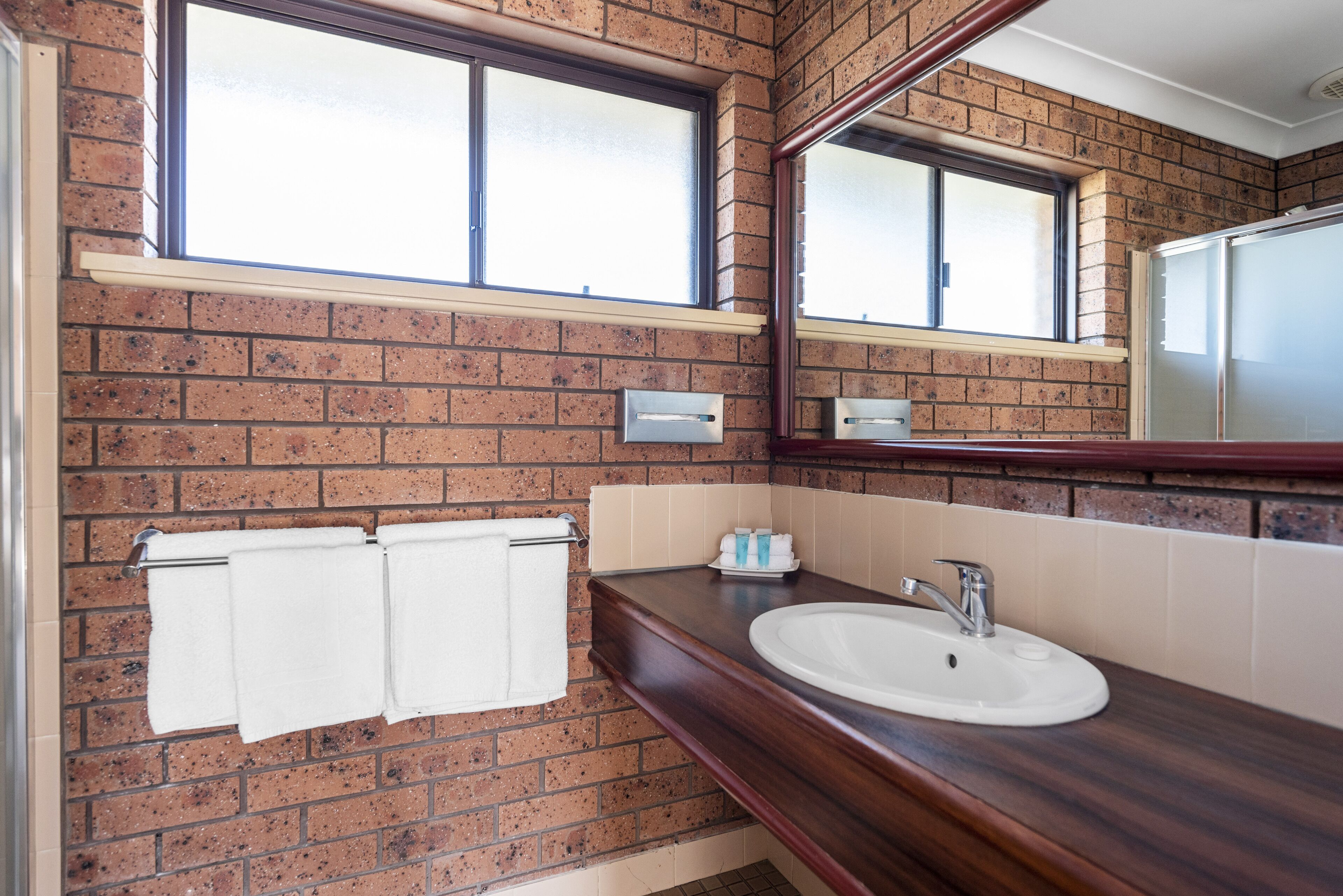 A bathroom with a brick wall, a window, a sink, and a mirror.