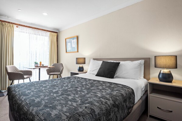 A hotel room with a bed, bedside tables, a chair, a small table with a plant, and a window with curtains.