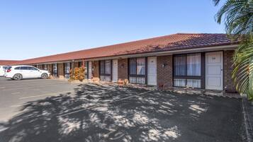Um motel com telhado de telhas vermelhas, quartos numerados e estacionamento.