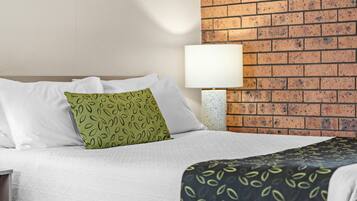 A hotel room with a brick wall, a bed with white bedding, a green pillow with a leaf pattern, and a black and green patterned throw.