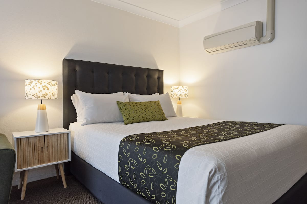 A neatly made bed with a dark headboard, two bedside lamps, and a green pillow.
