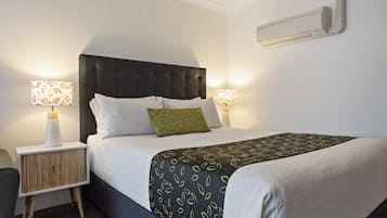 A neatly made bed with a dark headboard, two bedside lamps, and a green pillow.
