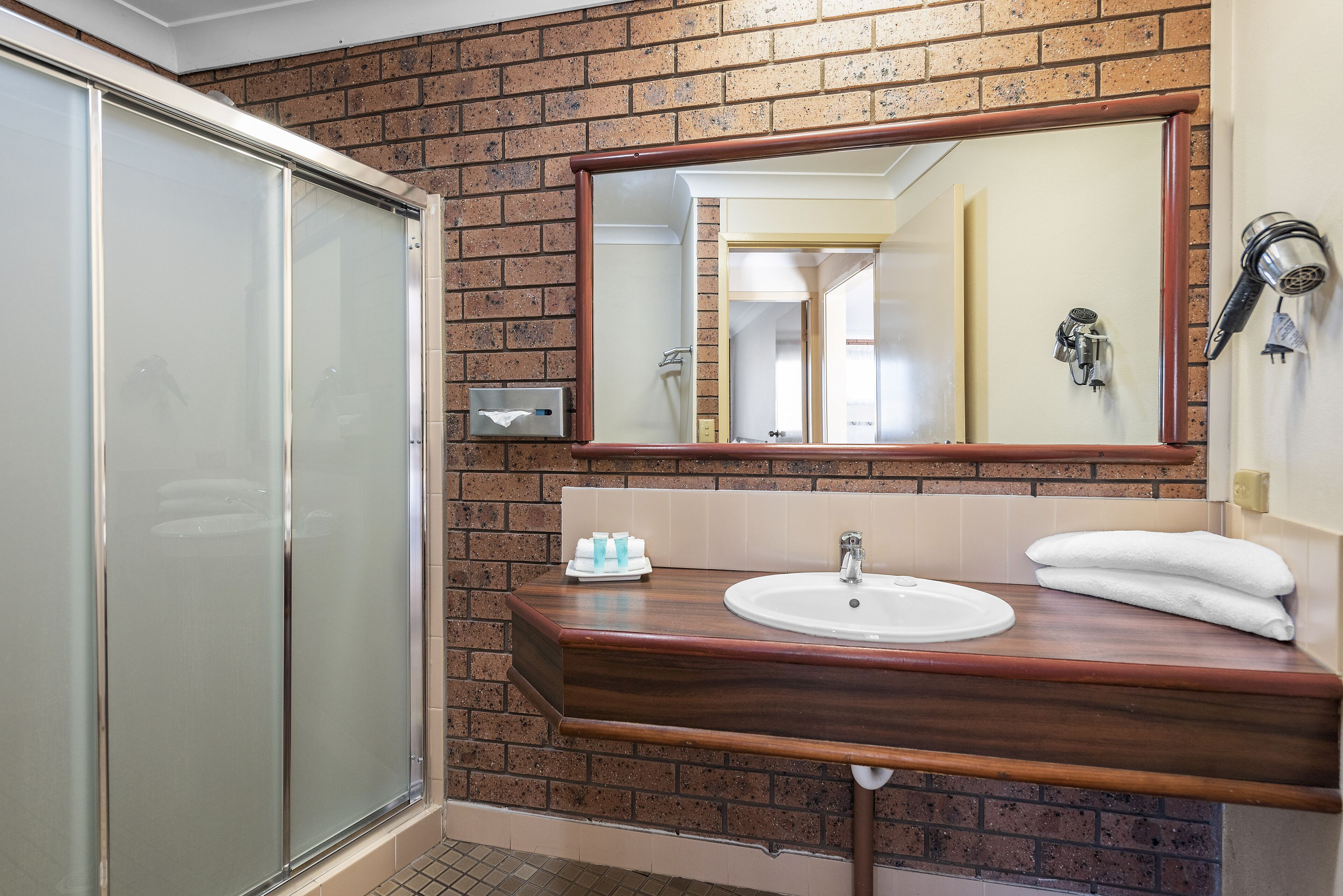 A bathroom with a wooden vanity, a sink, a mirror, and a shower area.