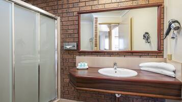 A bathroom with a wooden vanity, a sink, a mirror, and a shower area.
