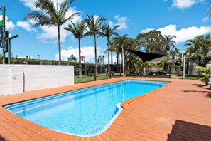 A swimming pool with a brick border, surrounded by palm trees and a fence.