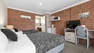 A hotel room with a brick wall, a bed with patterned bedding, a desk with a chair, a television, and a microwave.