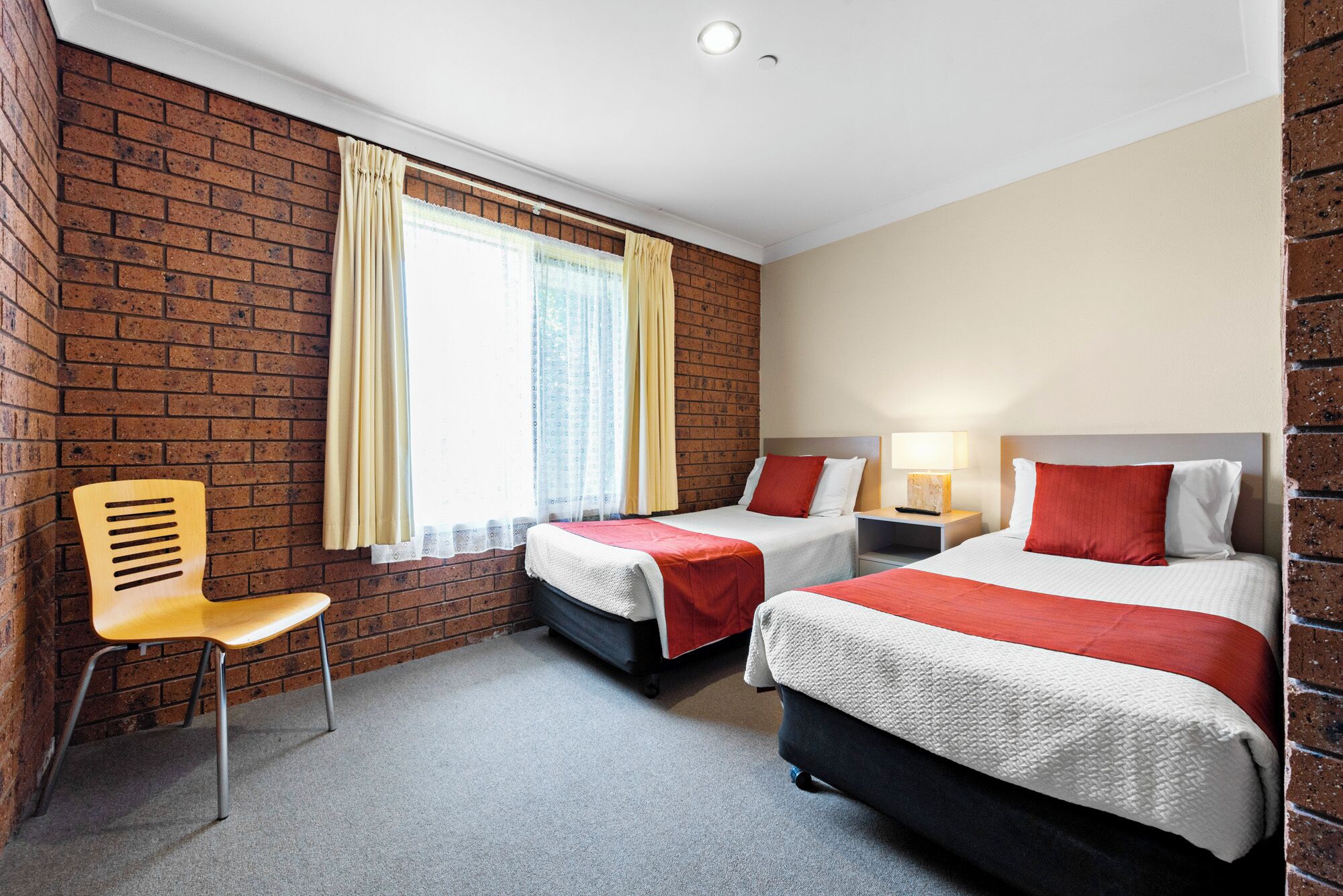 Habitació d'hotel amb dos llits, una cadira i una finestra amb cortines.