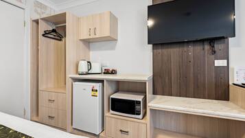 Habitación de hotel con cama, armario, refrigerador pequeño, microondas, cafetera y televisor de pantalla plana montado en la pared.