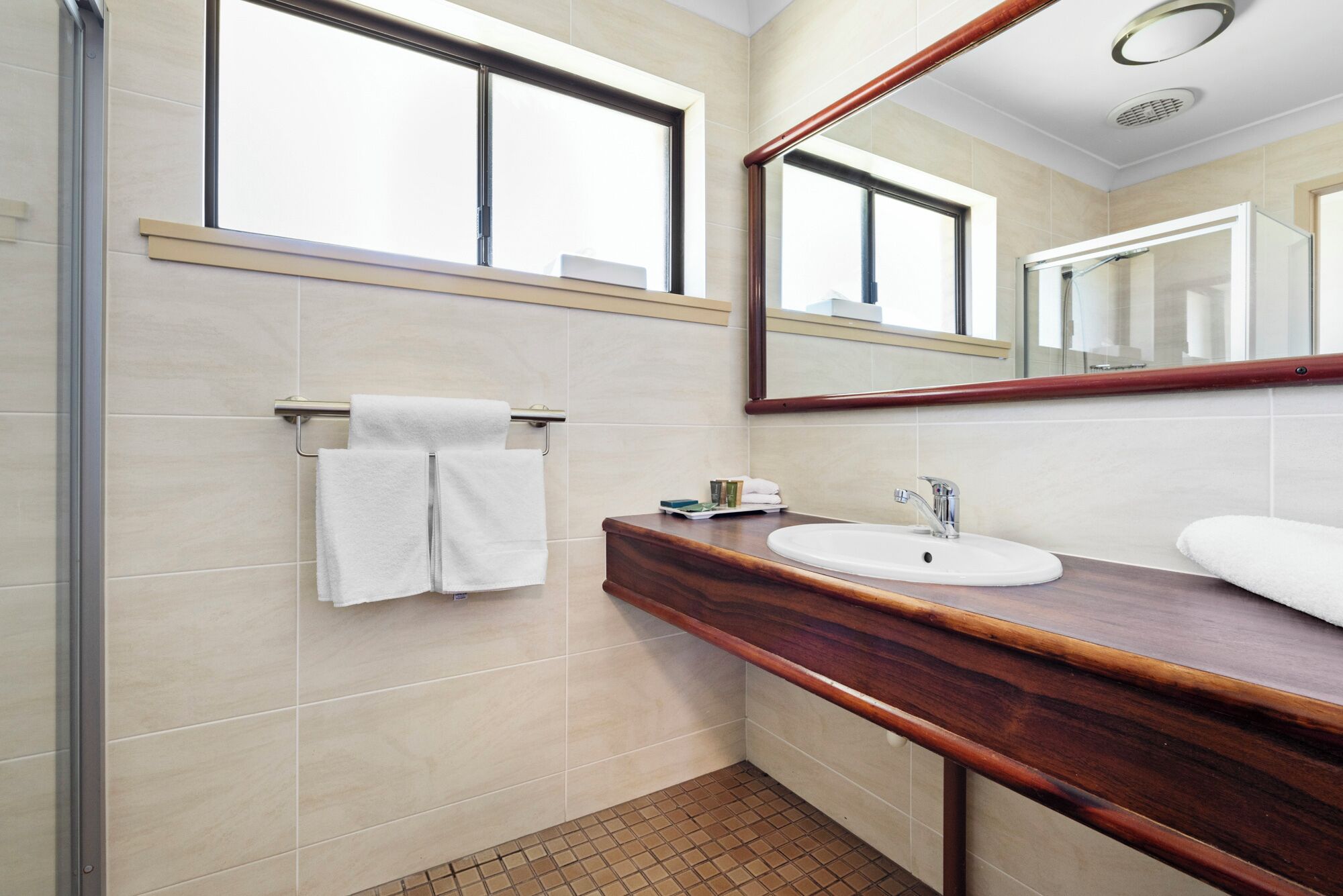 A modern bathroom with a wooden vanity, a white sink, and a large mirror.