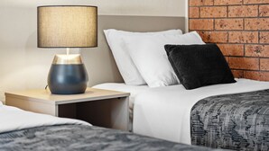 Una habitación de hotel con una cama, una mesita de noche con lámpara y una pared de ladrillo.