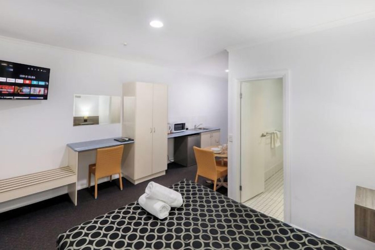 A hotel room with a bed, a desk, a chair, a television, and a wardrobe.