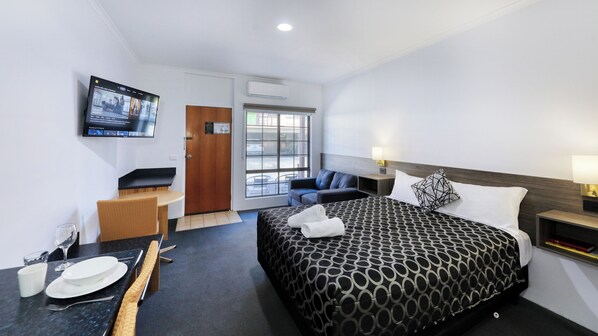 A hotel room with a bed, a TV mounted on the wall, a seating area with a table and chairs, and a window with a view of the street.