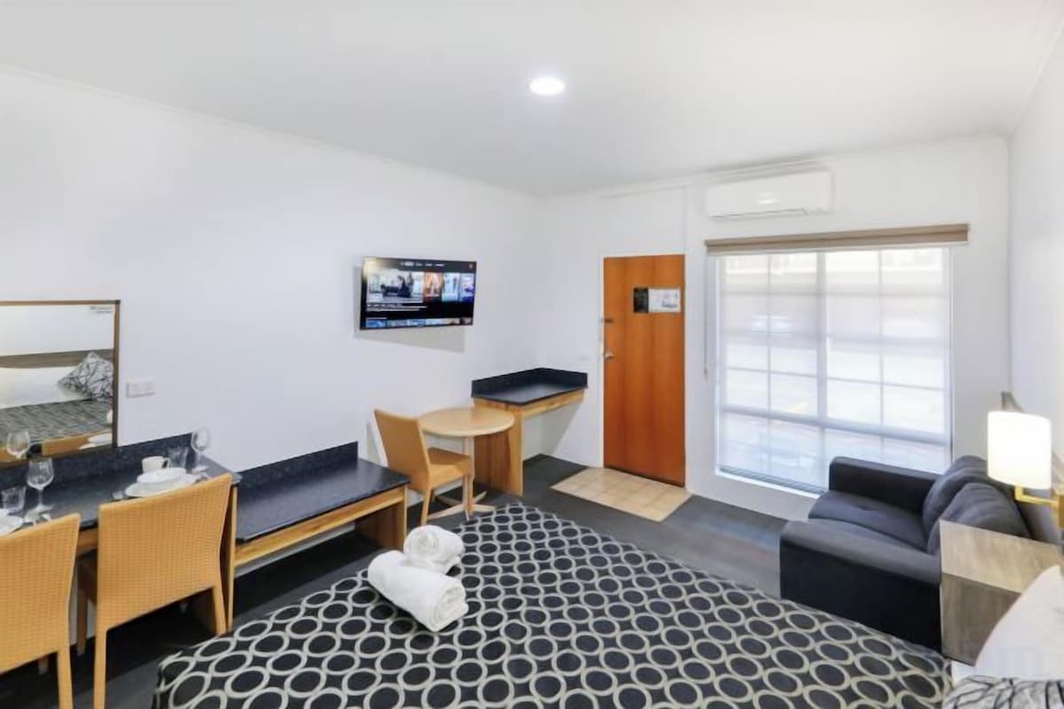 A hotel room with a bed, a desk, a chair, a sofa, and a television.