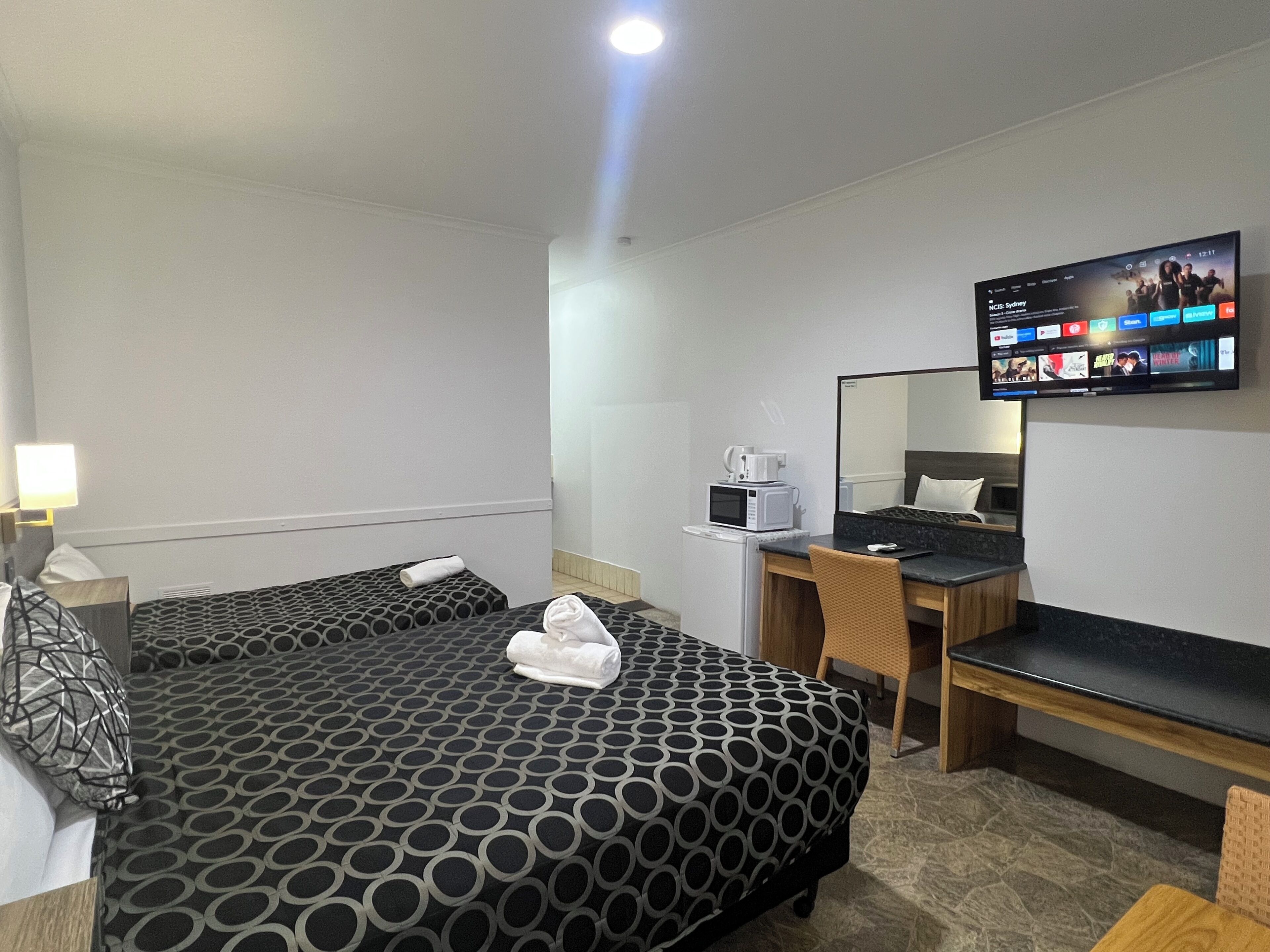 Habitación de hotel con dos camas, un escritorio con computadora, microondas y televisor de pantalla plana montado en la pared.
