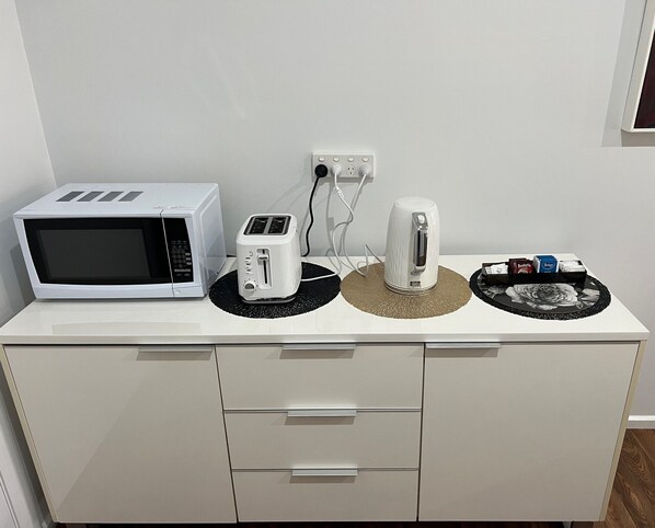 A kitchenette with a microwave, toaster, kettle, and a tray with tea bags. - The Cottage Motor Inn Albury CBD (South Albury)