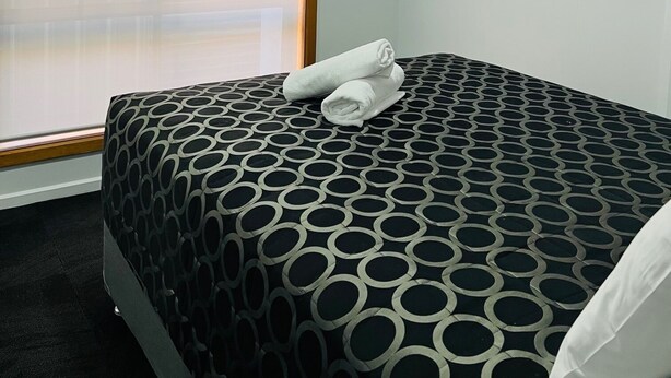 A hotel room with a large window, a bed with a patterned bedspread, and an air conditioning unit on the wall. - The Cottage Motor Inn Albury CBD (South Albury)