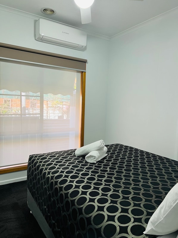 A hotel room with a large window, a bed with a patterned bedspread, and an air conditioning unit on the wall.