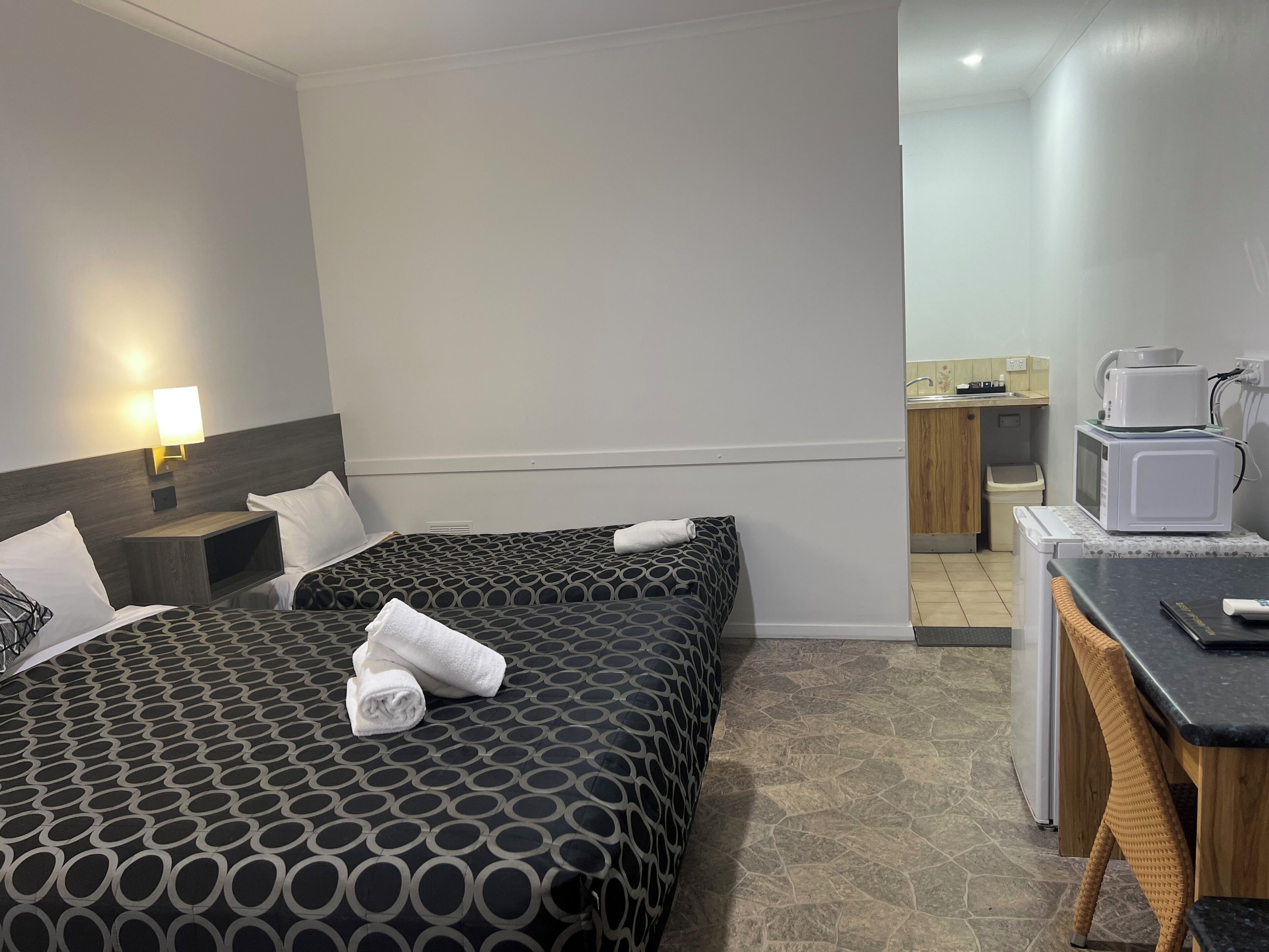 A hotel room with two beds, a desk with a microwave, and a small kitchenette.