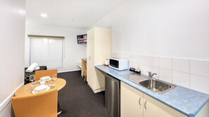 A compact kitchenette with a microwave, sink, and a dining area with a table and chairs. - The Cottage Motor Inn Albury CBD (South Albury)