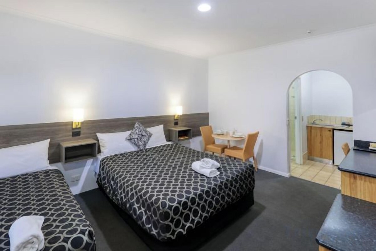 A hotel room with two beds, a desk, a chair, and a kitchenette.