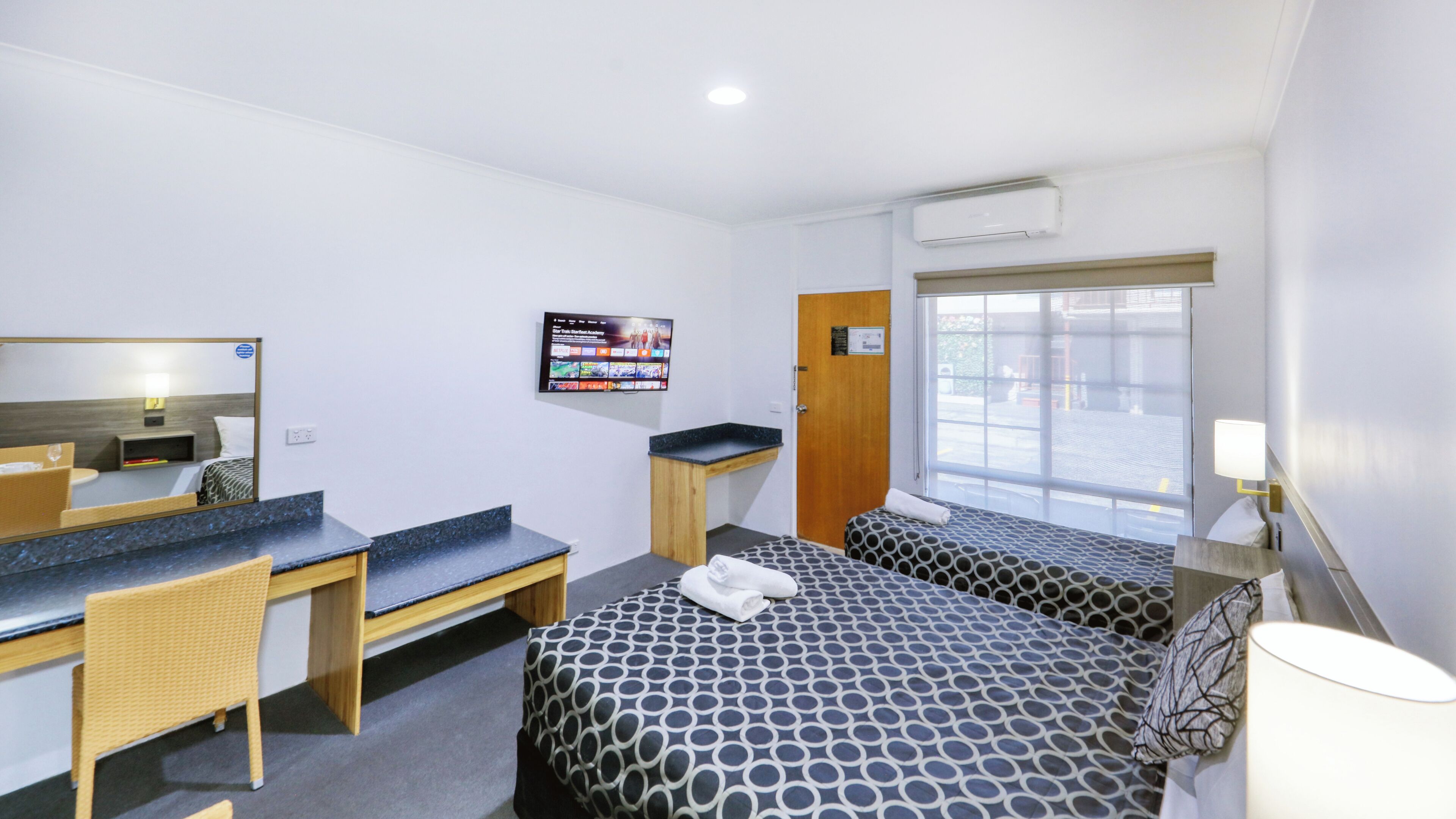 Habitación de hotel con cama, escritorio, silla, televisor montado en la pared y ventana.