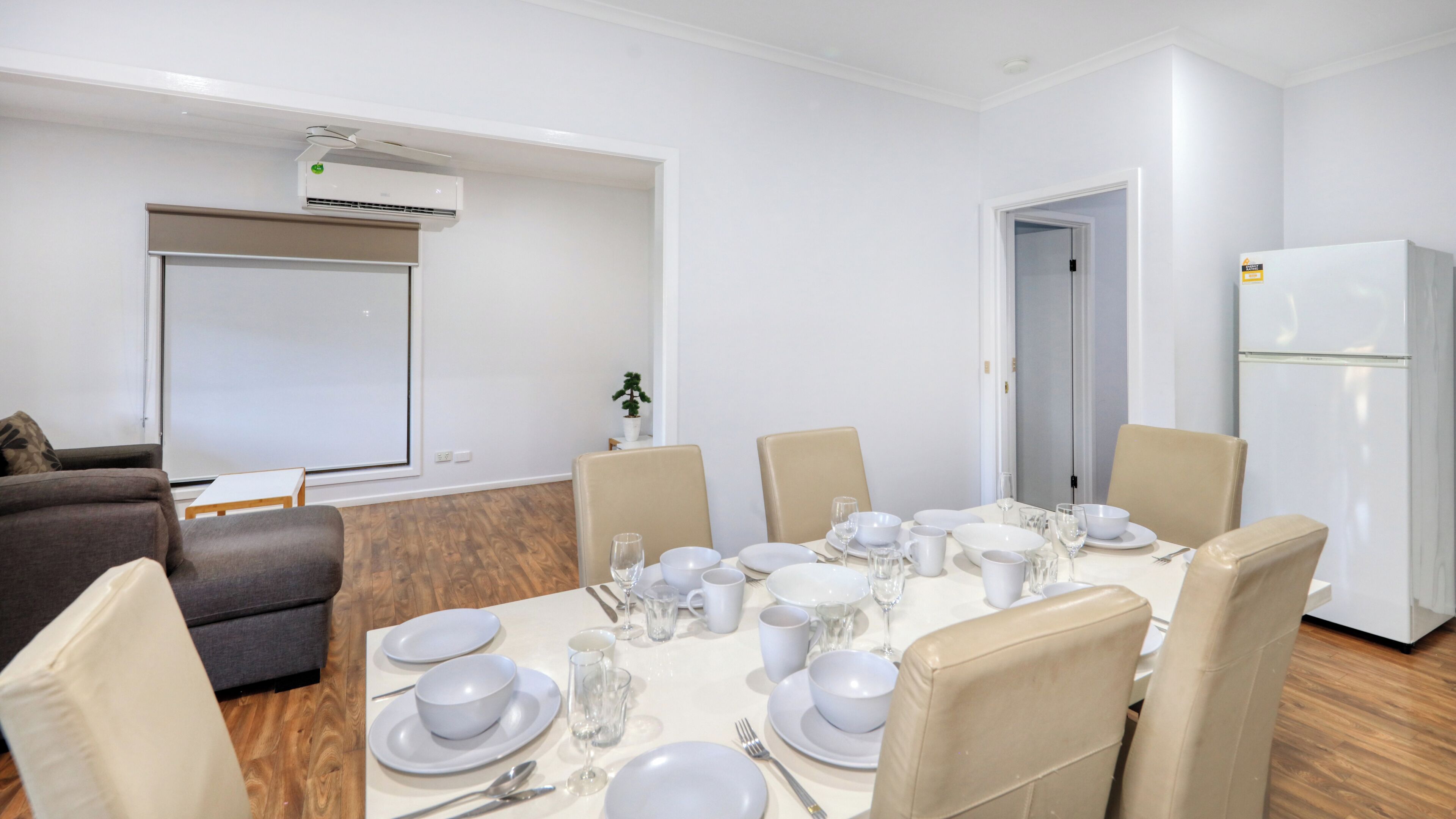 Una sala de conferències amb una taula blanca preparada per a una reunió, cadires beix i una pissarra blanca, a més d'una unitat de climatització blanca.