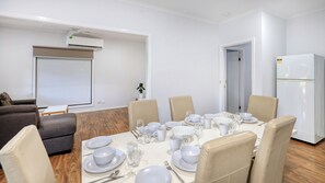 A conference room with a white table set for a meeting, beige chairs, a whiteboard, and a white air conditioning unit.