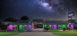 A motel with a starry night sky view, solar panels on the roof, and a sign indicating it's an owner-operated establishment.