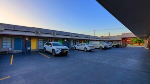 A parking lot with several cars and a building with multiple doors and air conditioning units.