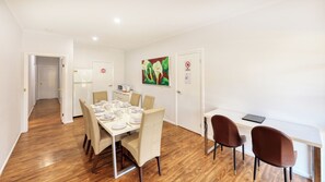 A dining area with a table set for six, a microwave, and a refrigerator. There are two chairs and a desk with a laptop.