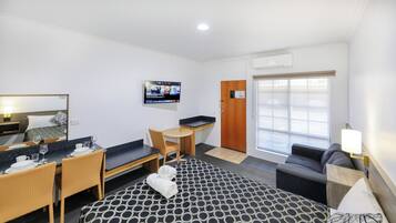 A hotel room with a bed, a desk, a chair, a sofa, a TV, and a window.