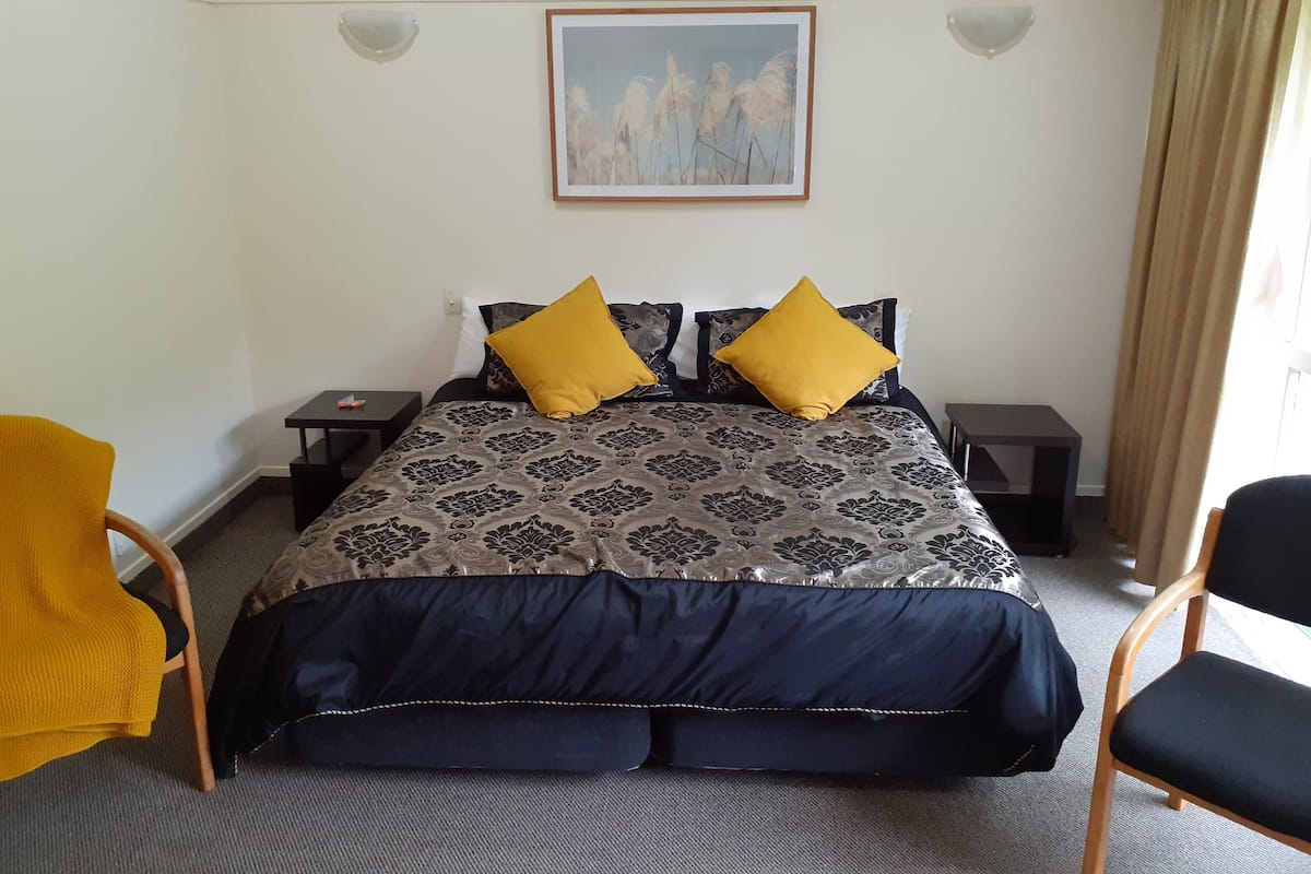 Ein Schlafzimmer mit einem Bett, zwei Nachttischen, einem Sessel und einem Bild an der Wand.