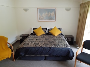 Un dormitorio con una cama, dos mesitas de noche, una silla y un cuadro en la pared.