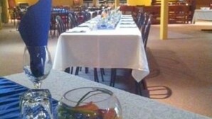 Comedor con mesas dispuestas para una comida, con un cuenco de vidrio decorativo y un portalápices azul.