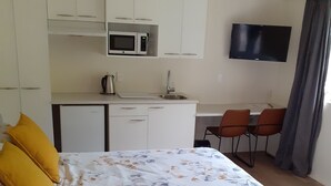 Un dormitorio con cama, un pequeño kitchenette, televisor y un escritorio con sillas.