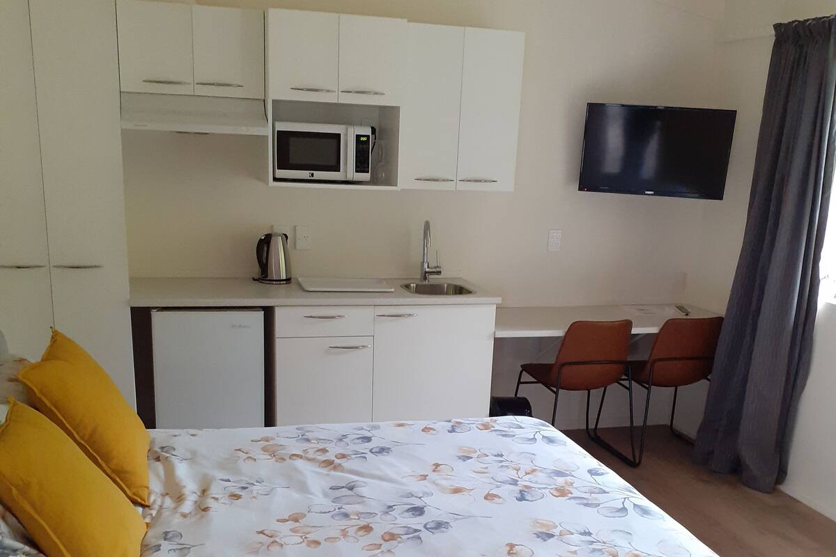 Ein Schlafzimmer mit Bett, einer kleinen Küchenzeile, einem Fernseher und einem Schreibtisch mit Stühlen.